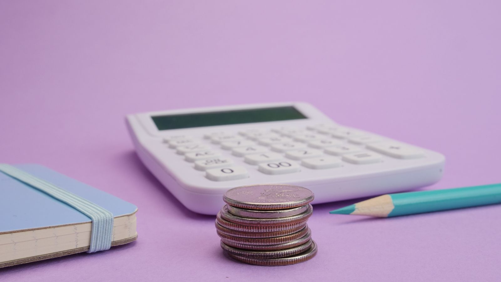 Pile de pièces, calculatrice blanche et carnet sur fond violet